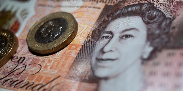 British currency in the form of two one pound coins rest atop a Bank of England ten pound note featuring an image of Queen Elizabeth II.