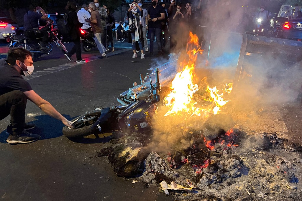 A police motorbike lies in the street next to burning debris during protests for Mahsa Amini