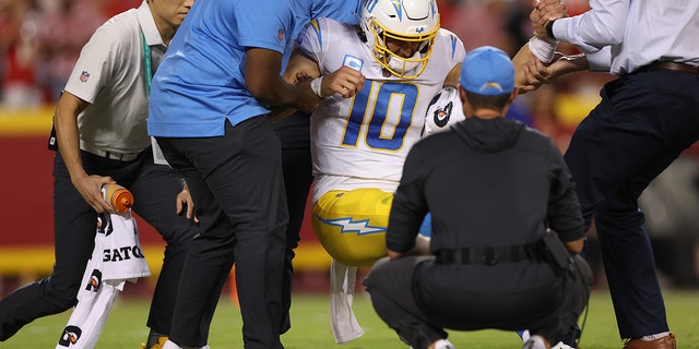 Justin Herbert #10 of the Los Angeles Chargers is helped off the field by the medical staff after being hit during the fourth quarter against the Kansas City Chiefs at Arrowhead Stadium on September 15, 2022 in Kansas City, Missouri.