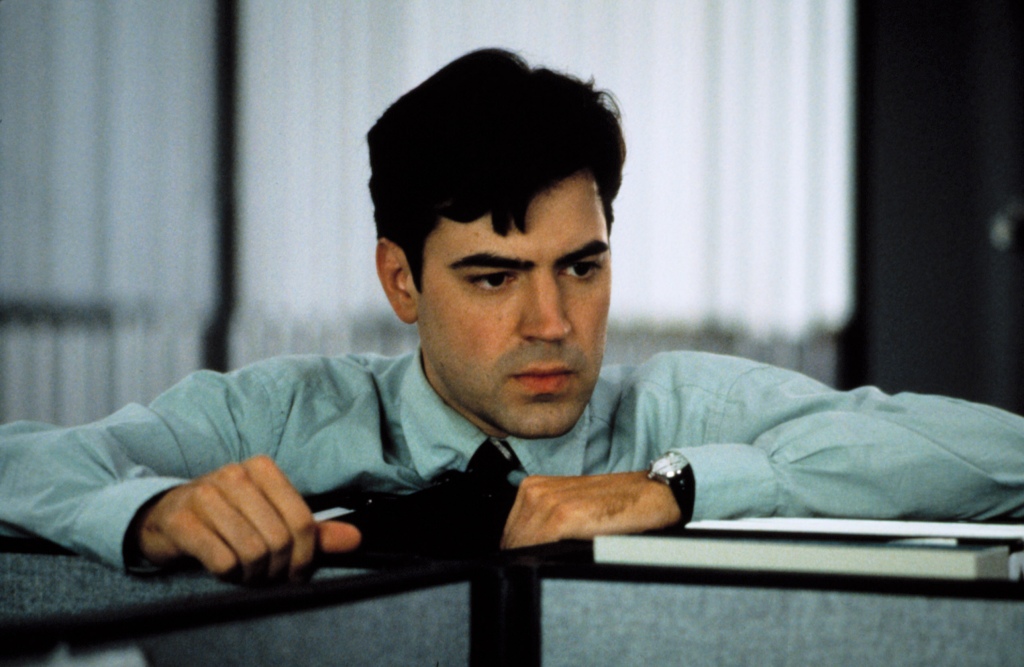 Photo of Ron Livingston as Peter in "Office Space." He's in his office and has his arms on the top of a desk and he's looking somewhat forlorn. He's wearing a green shirt and a black tie.