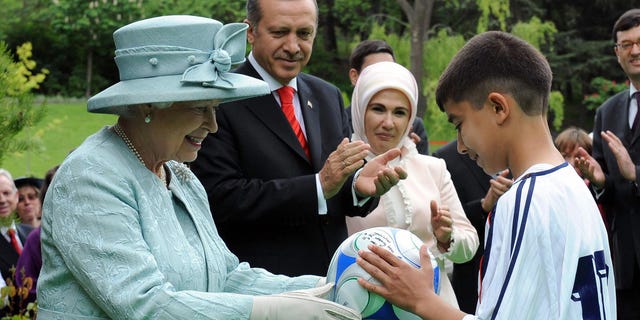 Britain's Queen Elizabeth II gives a soccer ball to a child as Turkey's Prime Minister Tayyip Erdogan and his wife Emine Erdogan watch at the British Embassy in Ankara on May 16, 2008.