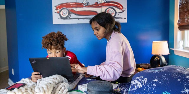 Fulton County Public Schools 8th grader, Ceani Williams, helps her 5th grade brother, Kareem Williams, with his classwork during a virtual learning day at their residence in Milton, Georgia.