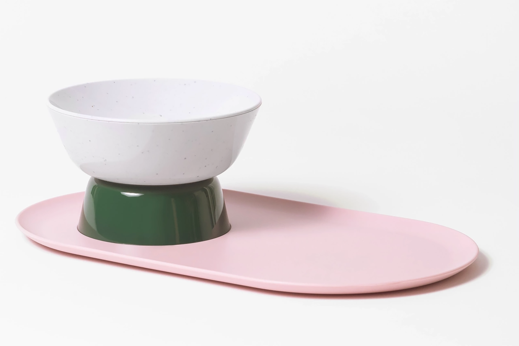 A pink tray with a white and green food bowl for a pet on top 