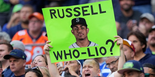 A fan holds up a sign with a photo of Seattle Mariners MLB baseball outfielder Julio Rodriguez that reads "Russell Who-Lio?" in reference to the status in Seattle of former Seattle Seahawks quarterback Russell Wilson, who now plays for the Denver Broncos, during the first half of an NFL football game between the Seahawks and Broncos, Monday, Sept. 12, 2022, in Seattle.