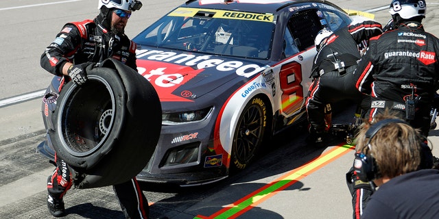 A crew member for Tyler Reddick's No. 8 car, left, carries a damaged tire away during a pit stop at a NASCAR Cup Series auto race at Kansas Speedway in Kansas City, Kan., Sunday, Sept. 11, 2022.