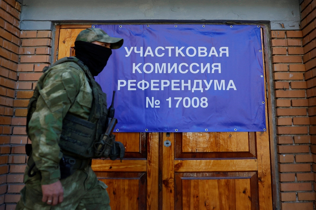 A service member of the self-proclaimed Donetsk People's Republic walks past a banner on the doors of a polling station ahead of the planned referendum on the joining of the Donetsk people's republic to Russia on Sept. 22, 2022 in Donetsk, Ukraine. The banner reads: "District сommission of referendum no. 17008".