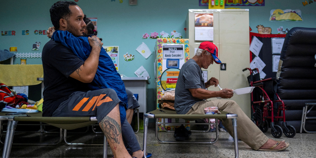 A man who was evacuated from his home embraces a girl in a classroom of a public school turned shelter as Hurricane Fiona and its heavy rains approaches in Guayanilla, Puerto Rico September 18, 2022.