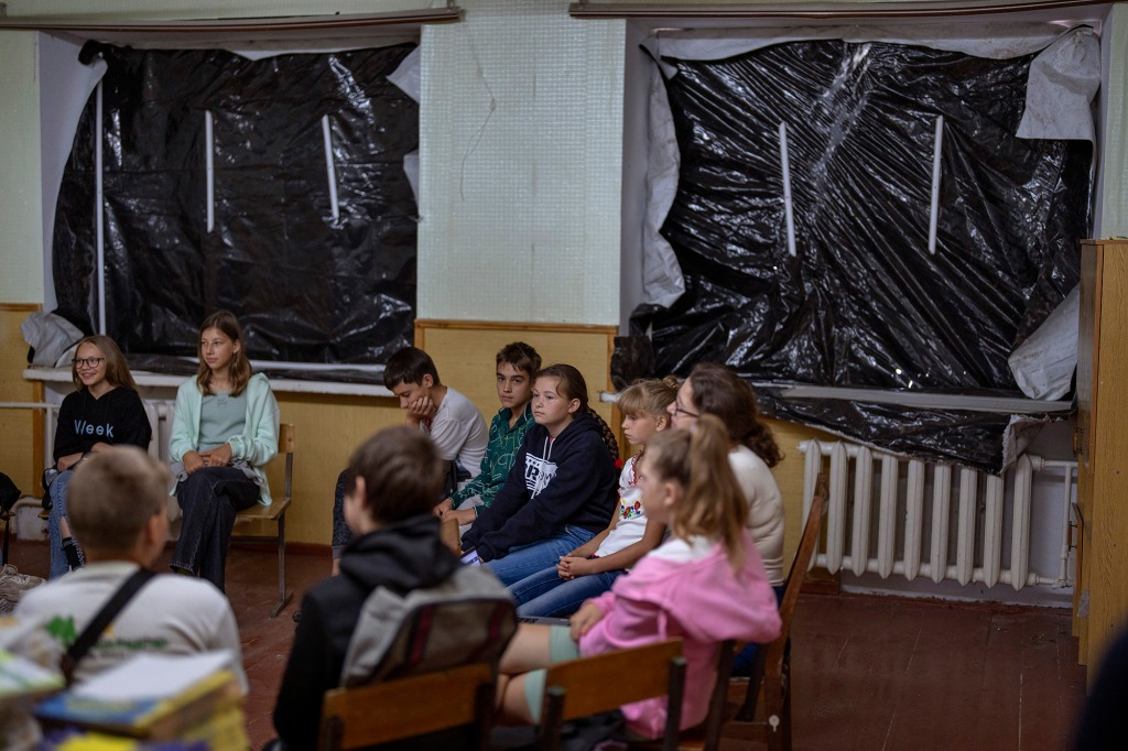 Students sit in a blast-damaged classroom.