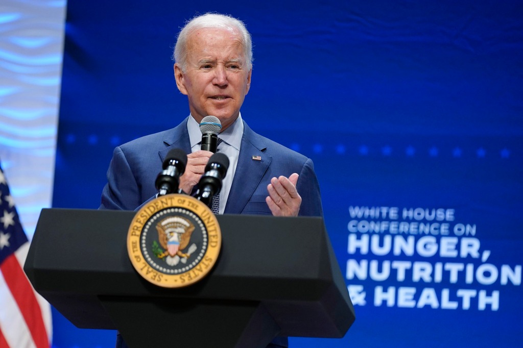 President Biden is shown behind a podium with a microphone in his hand, addressing a crowd during a White House event on nutrition
