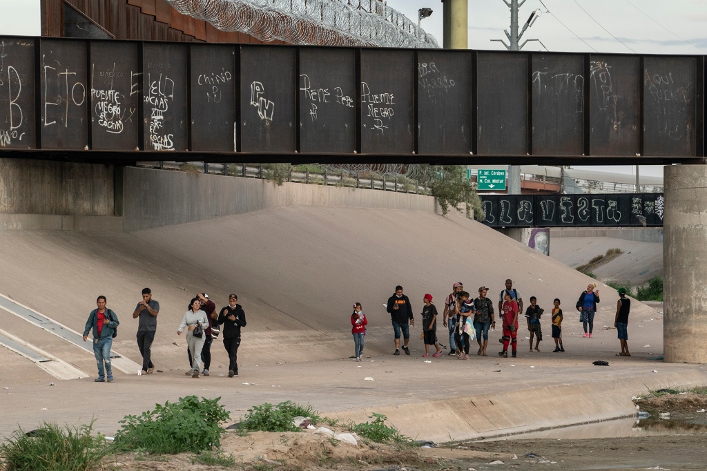 Asylum-seeking migrants walk by the border wall in El Paso, Texas on Sept. 25, 2022.