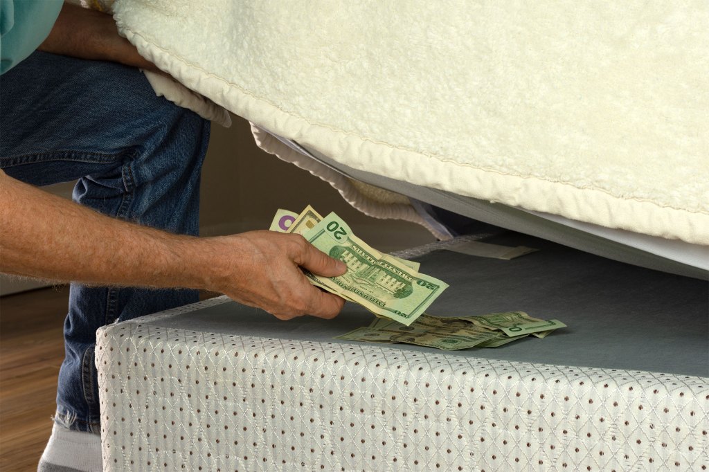 Man putting money under his mattress to save it showing no trust in financial institutions and banks.