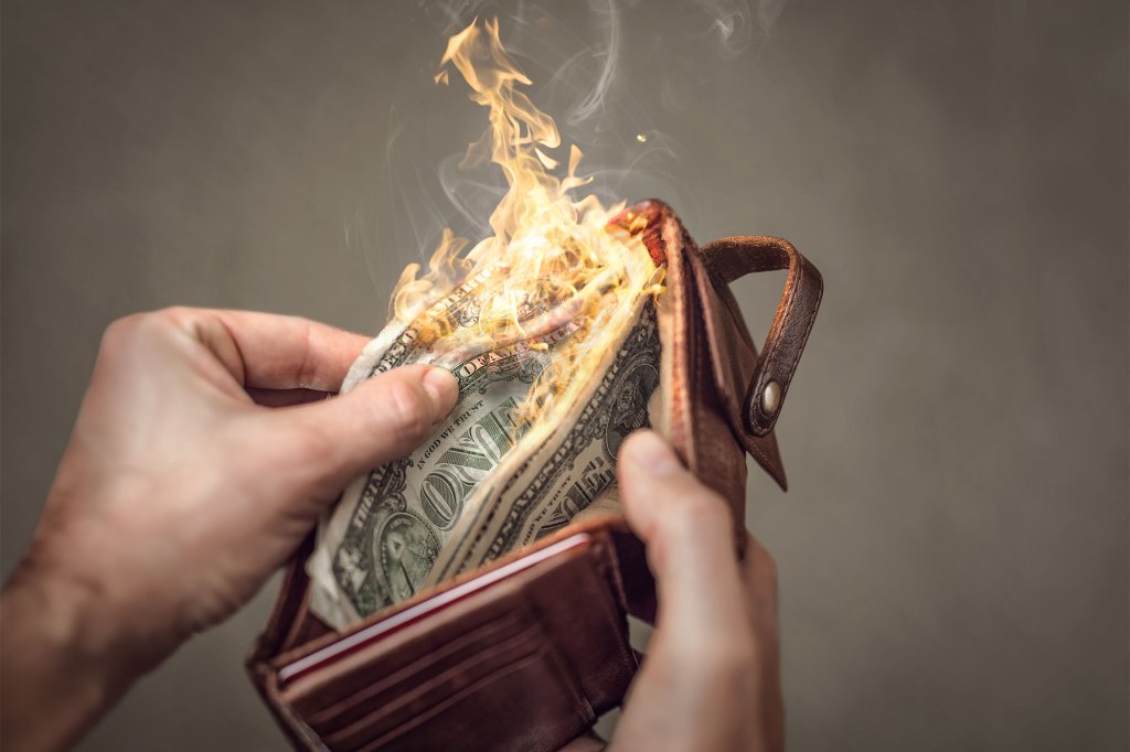 Hands holding a wallet with US dollar bills on fire.