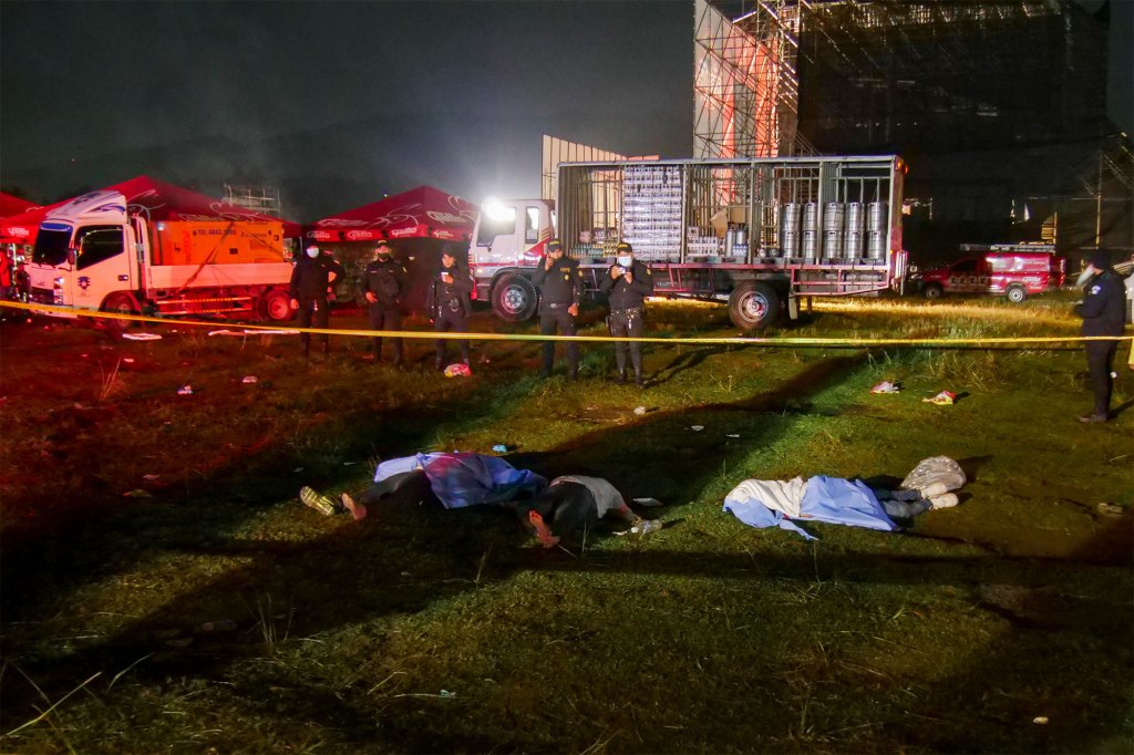 Firefighters and police stand next to the bodies of people who died in a stampede during an outdoor concert for Independence Day celebrations in Quetzaltenango, Guatemala,