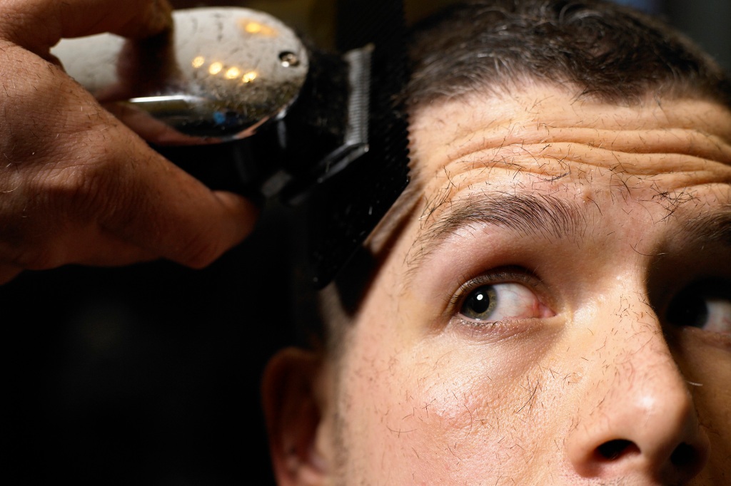 Barber shaving man's hair with electric razor, close-up