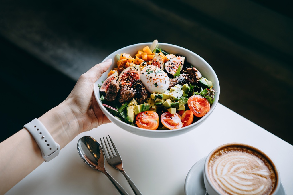 Close up of woman's hand holding a bowl of fresh beef cobb salad,