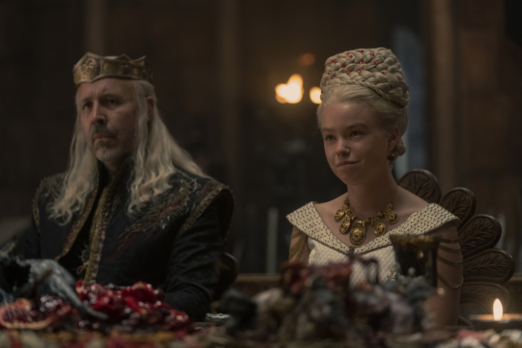 King Viserys (Paddy Considine) and Rhaenyra (Milly Alcock) at her wedding feast sitting at a table. 