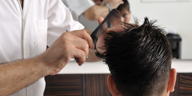 A barber cuts a child's hair with scissor at a barbershop.