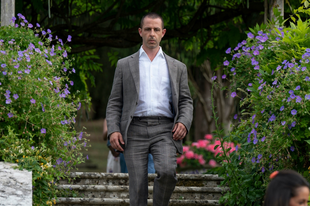 Jeremy Strong wearing a suit walking through a garden. 