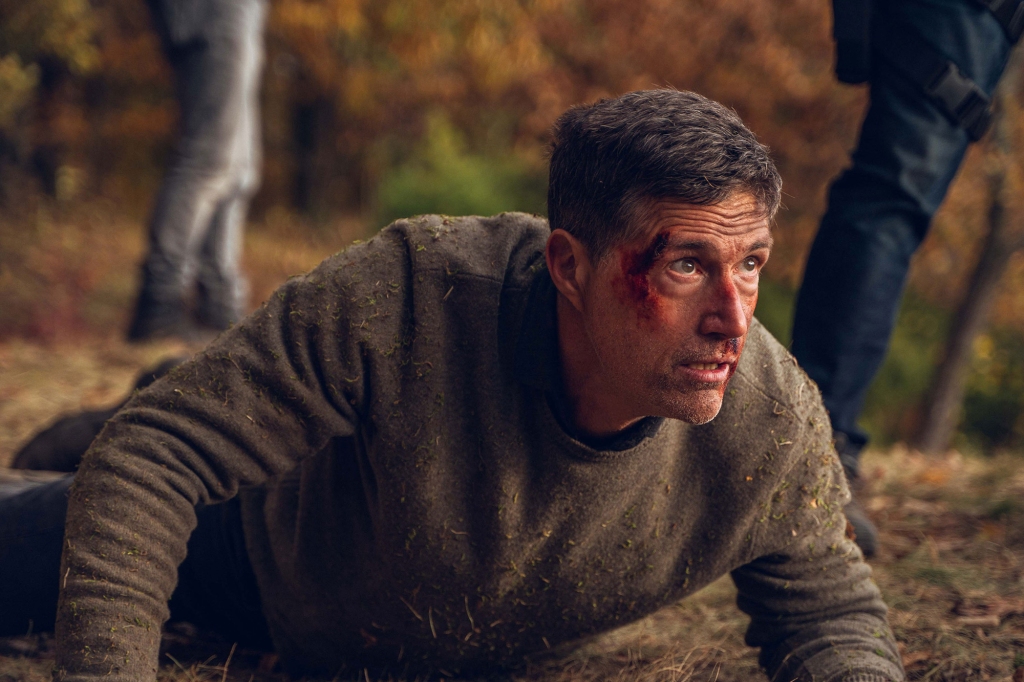 Matthew Fox lying on the ground in the woods looking bloody and worried. 