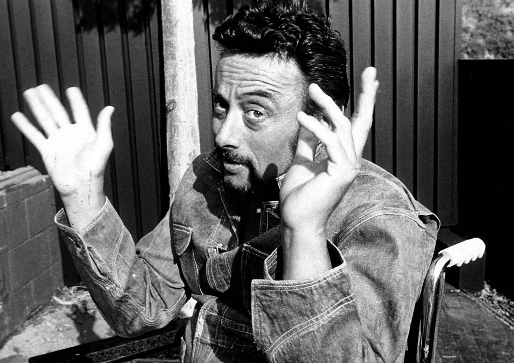 Lenny Bruce poses with his hands up. 