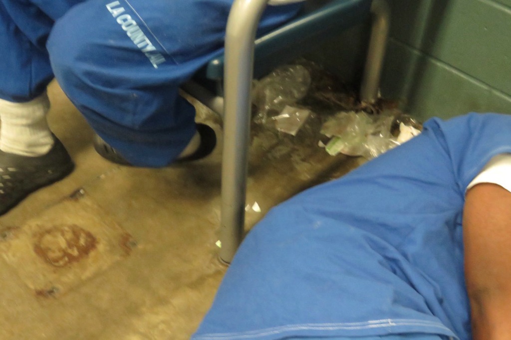 An inmate sleeps next to garbage on the ground in horrifying living conditions. 