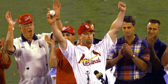 Mark McGwire(C) of the St. Louis Cardinals holds the ball he hit for his 62nd home run of the season against the Chicago Cubs, which was given to him by Tim Forneris(2ndL), as father John McGwire(L), Roger Maris Jr.(2ndR) and Kevin Maris look on 08 September at Busch Stadium, in St Louis, MO. McGwire broke the home run record of 61 home runs for the season set by Roger Maris in 1961.