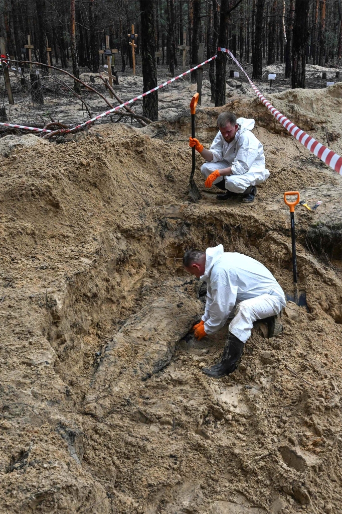 Two forensic technicians dig up a body in a forest on the outskirts of Izium, eastern Ukraine on Sept. 16, 2022.