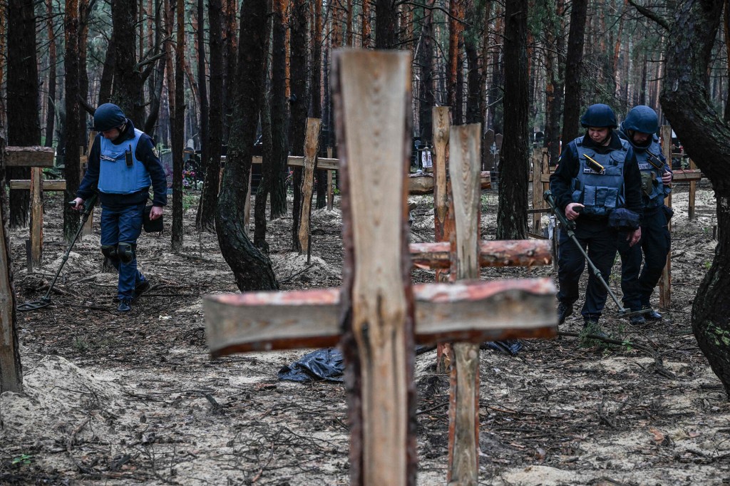 Two forensic technicians carry a body bag in a forest on the outskirts of Izyum, eastern Ukraine on September 16, 2022.