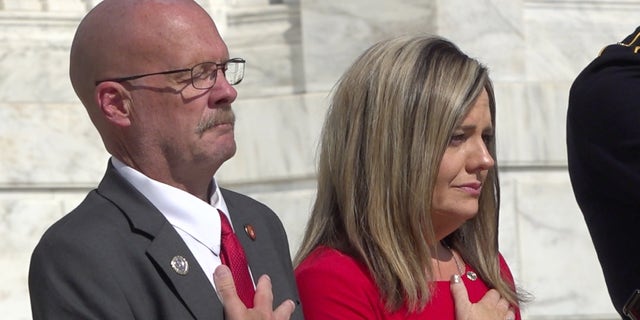 Darin Hoover and Kelly Barnett place their hands over their hearts at the wreath ceremony for Taylor at the Tomb of the Unknown Soldier in Arlington National Cemetery on Aug. 26, 2022. 