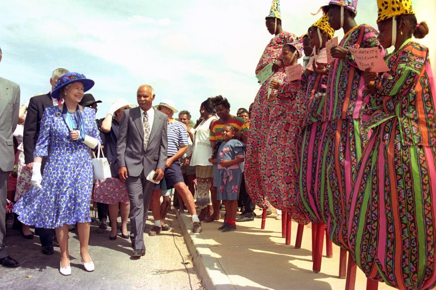 Though she had a broken wrist during her 1994 visit to Anguilla, Queen Elizabeth kept calm and carried on while greeting local dancers.