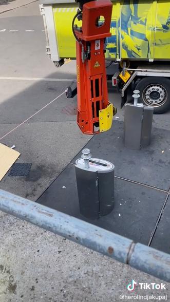 The machine's arm is shown pulling on a relatively small pole to unearth a huge metal container filled with the public’s garbage.