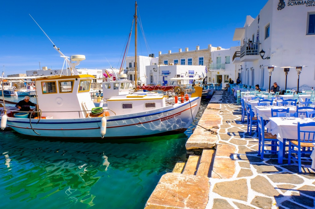 Fishboat and restaurant tables on the harbour. Naoussa village