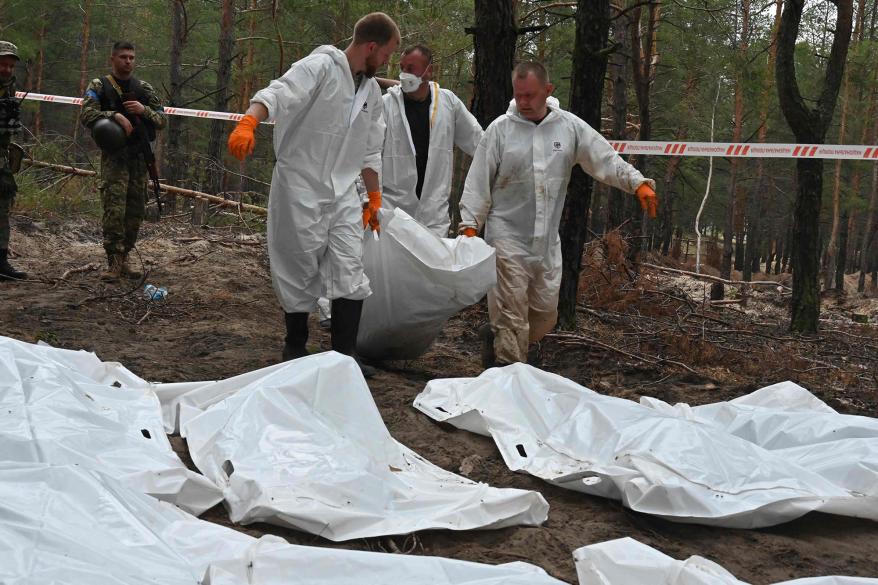 Forensic technicians carry a body bag in a forest outside the city of Izium.