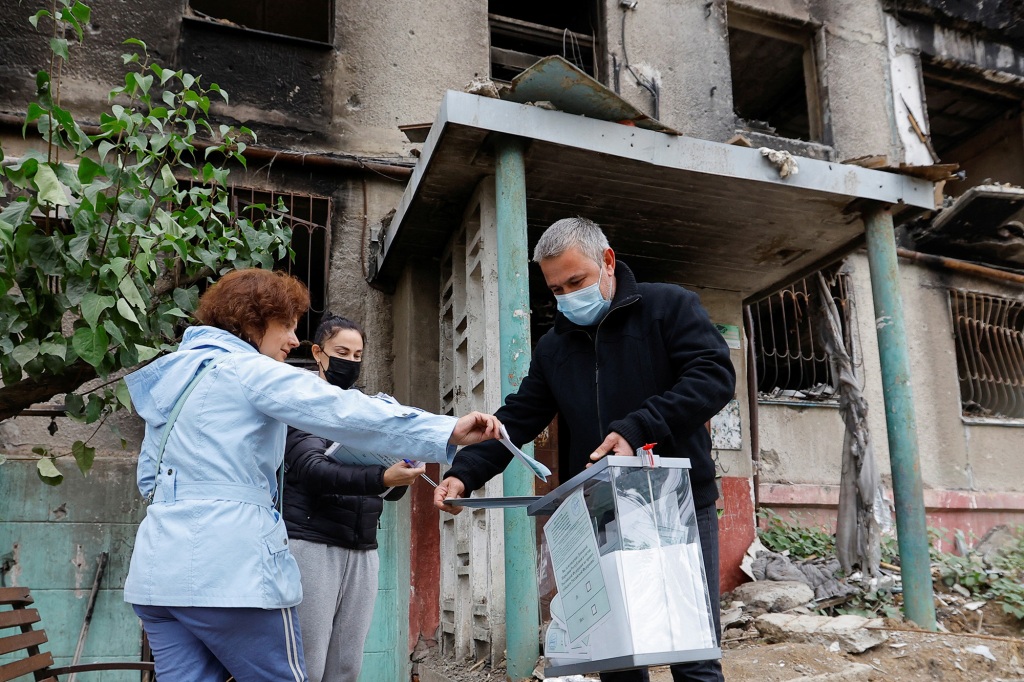 A local resident casts a ballot into a mobile ballot box carried by members of an electoral commission