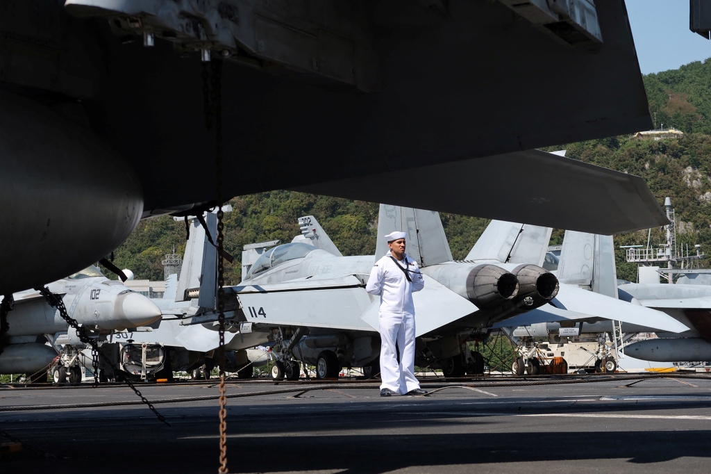 A crew member stands in front of U.S. Navy F/A-18 jets that sit on the deck of the USS Ronald Reagan as it is anchored at a port in Busan, South Korea on Sept. 23, 2022.