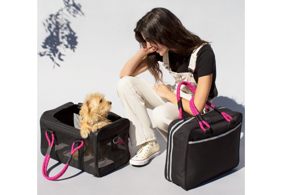 A woman bends over to look at her dog in a black and pink carrier 