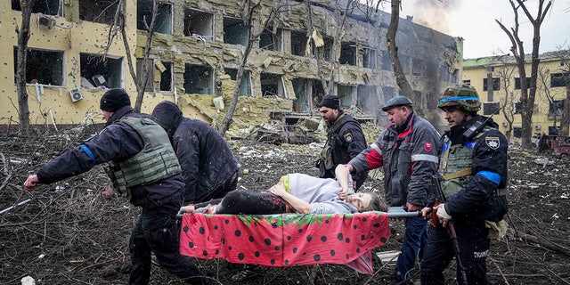 Ukrainian emergency employees and volunteers carry an injured pregnant woman from the damaged by shelling maternity hospital in Mariupol, Ukraine, 