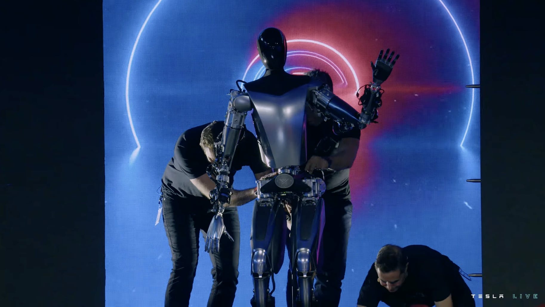 A picture of a Tesla robot being supported on stage by three engineers. 