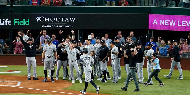 New York Yankees' Aaron Judge (99) approaches home plate as the teammates come out to congratulate him after hitting a solo home run, his 62nd of the season, in the first inning of the second baseball game of a doubleheader against the Texas Rangers in Arlington, Texas, Tuesday, Oct. 4, 2022. With the home run, Judge set the AL record for home runs in a season, passing Roger Maris.