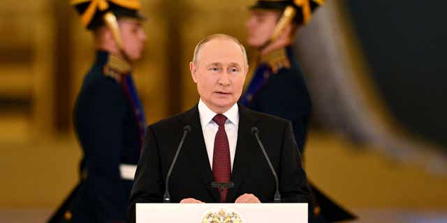 Vladimir Putin delivering an address flanked by men in military uniforms.