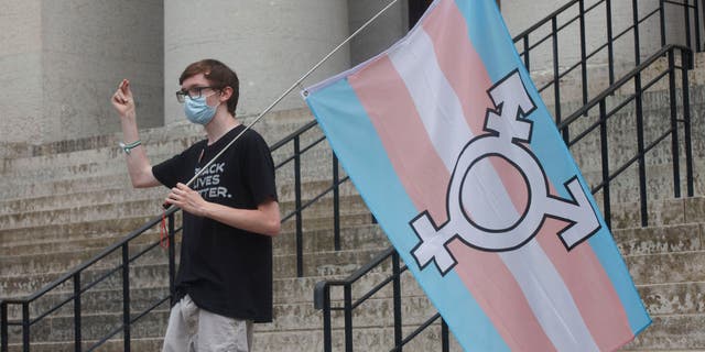 A protester holds the trans flag and snaps in solidarity with other speakers during a demonstration at the Ohio Statehouse in Columbus, Ohio, on June 25, 2021.