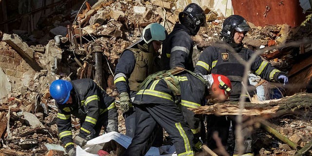 Firefighters help a local woman evacuate from a residential building destroyed by a Russian strike using an Iranian-made drone, in Kyiv, Ukraine Oct. 17, 2022.