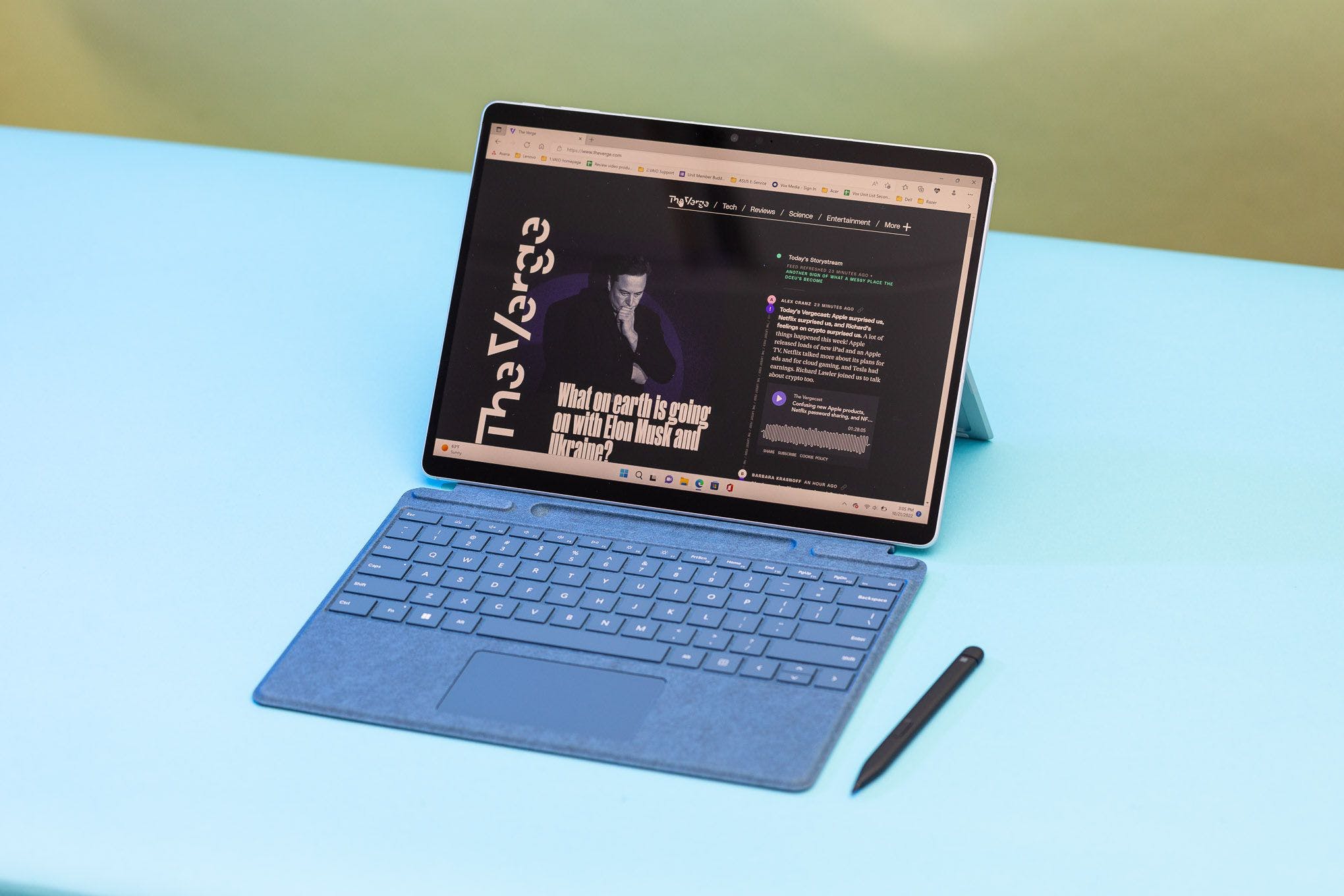 The Surface Pro 9 in laptop mode seen from above with the stylus beside it. The screen displays The Verge homepage.