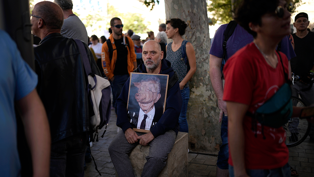 A protester hold a photo of a millionaire with a pig face before a demonstration, Tuesday, Oct. 18, 2022 in Marseille, southern France. France is in the grip of transport strikes and protests for salary raise on Tuesday that threaten to dovetail with days of wage strikes that have already hobbled fuel refineries and depots, sparking chronic gasoline shortages around the country.