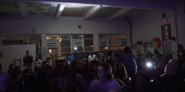 Attendees at Rep. Alexandria Ocasio-Cortez's town hall pull out their phones after the lights go out.