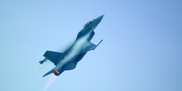 An F16 airplane going up in the sky, outburner visible.