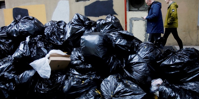 People make their way past trash bags on Oct. 18, 2022 in New York City. In an effort to deter rats and keep the area from seeming too dirty, New Yorkers will have to wait until 8 p.m. to dump their trash out.