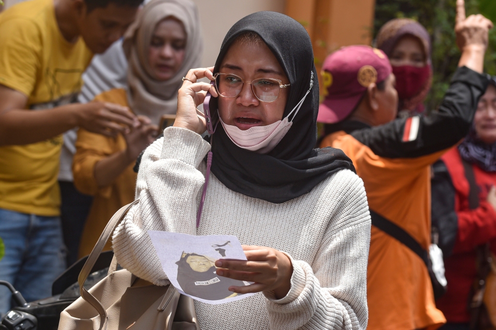 A women makes a phone call as she holds a picture of a victim at a hospital in Malan Indonesia.