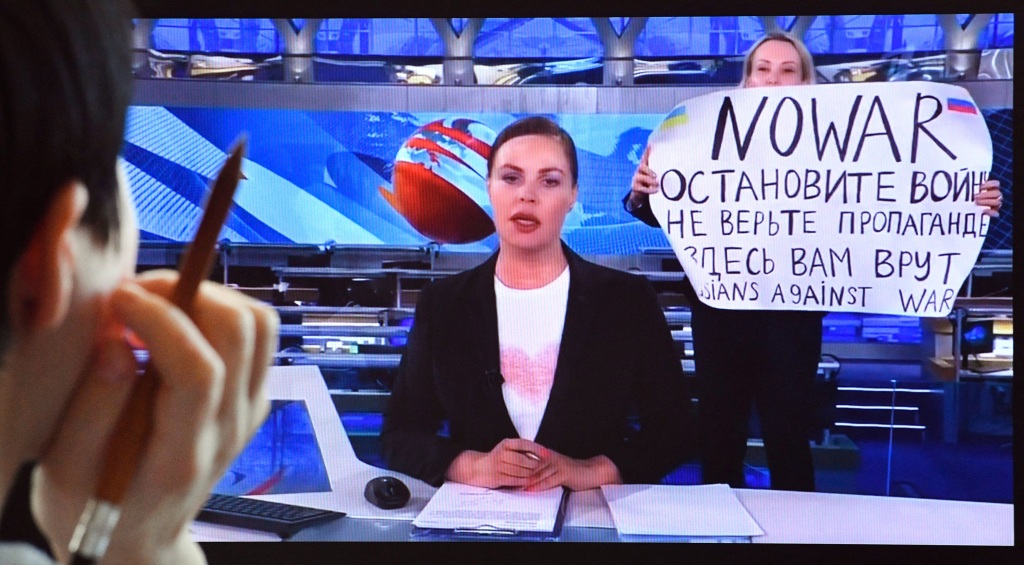 A woman looks at a computer screen watching a dissenting Russian Channel One employee entering Ostankino on-air TV studio during Russia's most-watched evening news broadcast, holding up a poster which reads as "No War" and condemning Moscow's military action in Ukraine in Moscow on March 15, 2022. 
