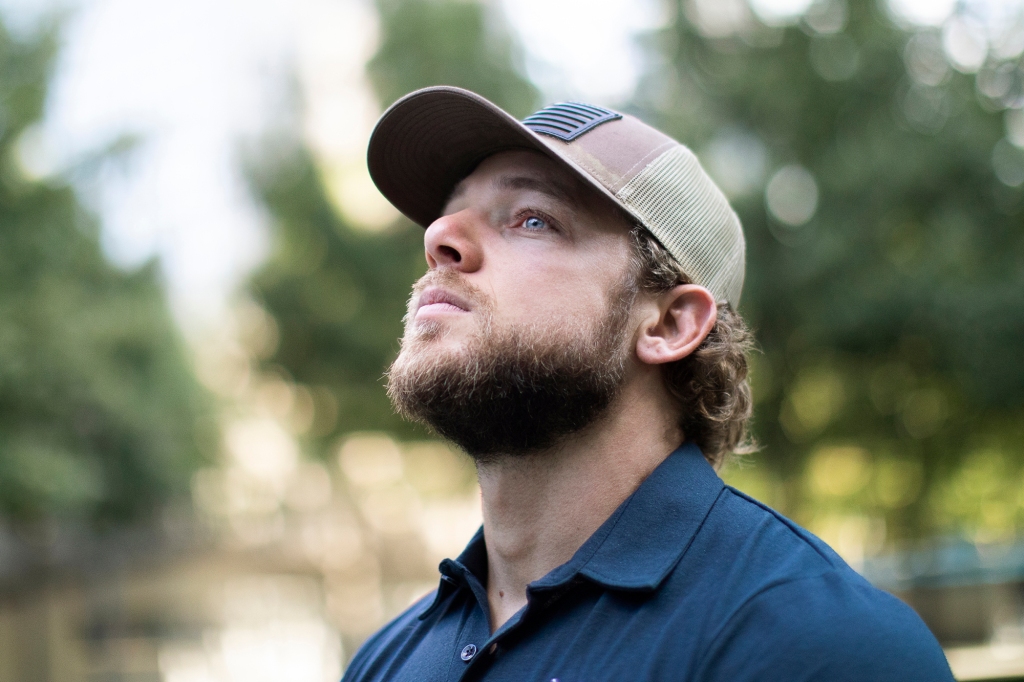 Photo of Max Thieriot as Clay Spenser in "SEAL Team." He's wearing a baseball cap and a blue shirt and is gazing wistfully up at the sky.